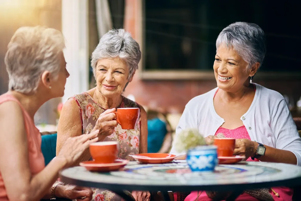 A group of older adult friends sitting in a restaurant happily talking and enjoying coffee, symbolizing how ai hearing aids help with speech clarity even in challenging listening environments