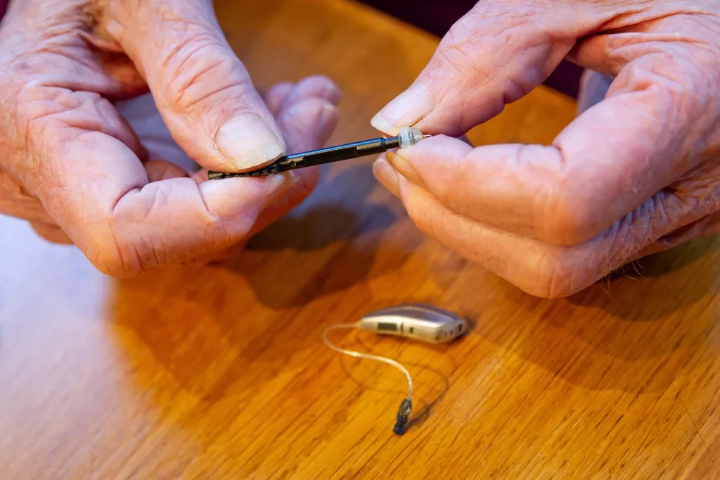 An above view of an older adult sitting at a table cleaning their hearing aids, demonstrating the importance of proper hearing aid cleaning and maintenance.
